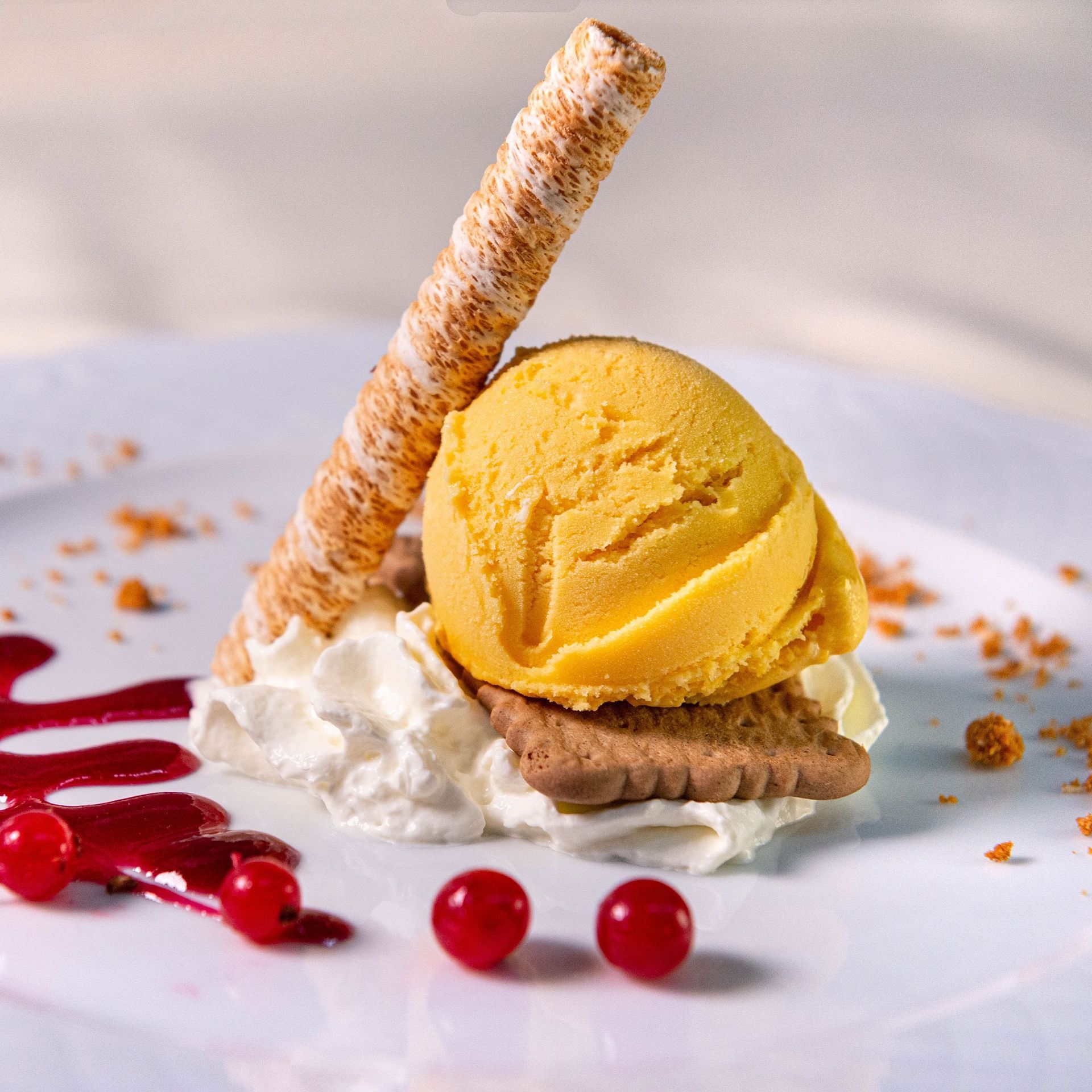 Sorbete de mango con crema batida, barquillo enrollado y salsa de frambuesa en un plato blanco.