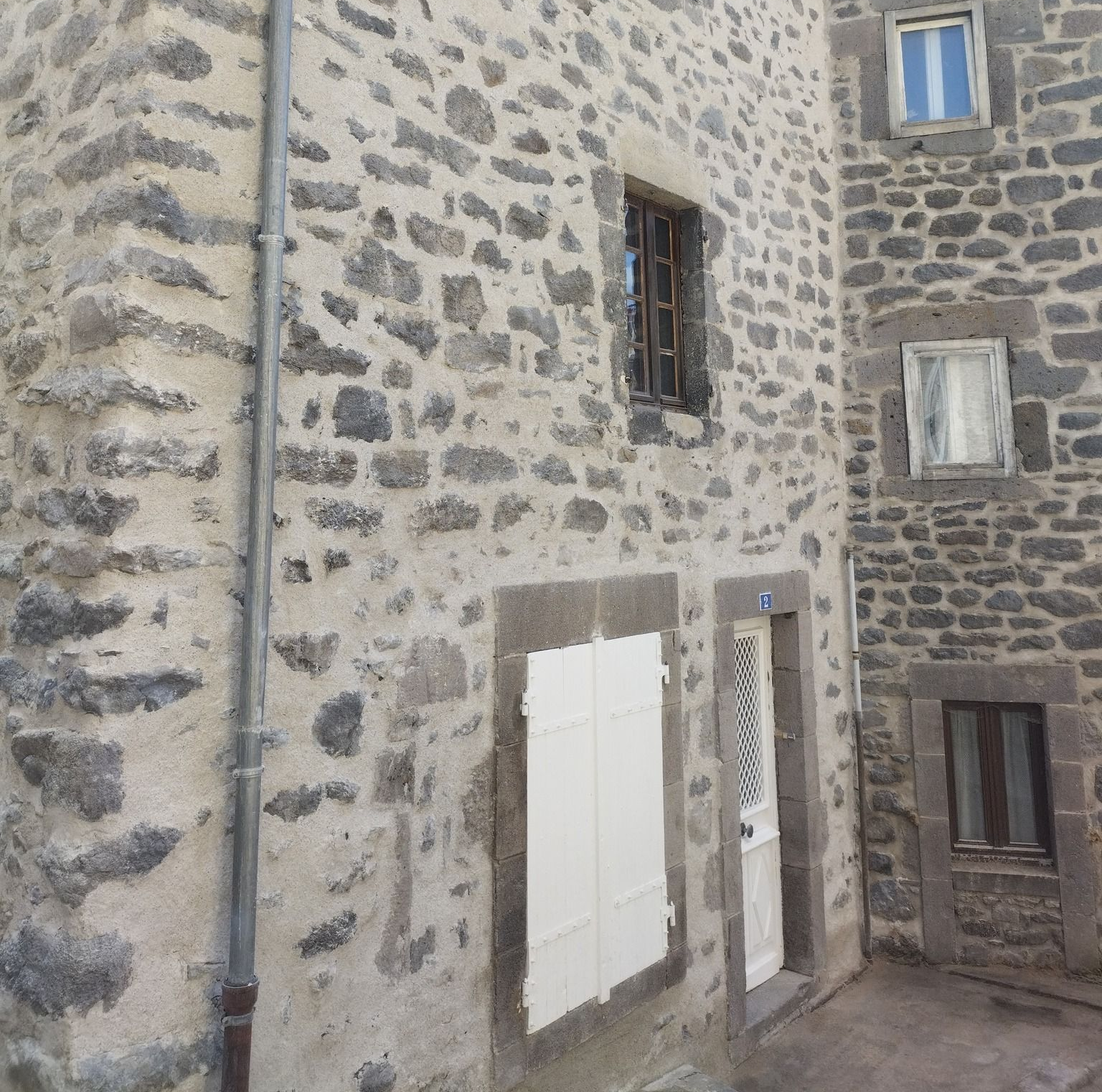 Bâtiment en pierre avec de nombreuses fenêtres et des volets blancs.