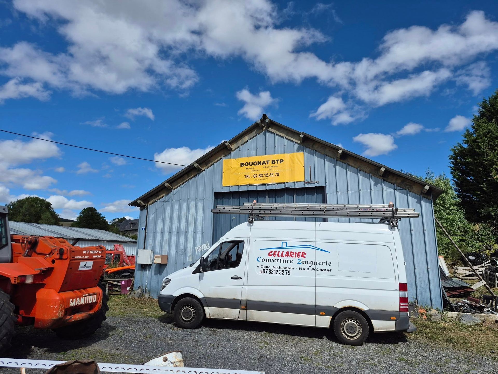 Une camionnette blanche est garée devant un hangar bleu. Un pont élévateur orange et du matériel se trouvent à gauche.