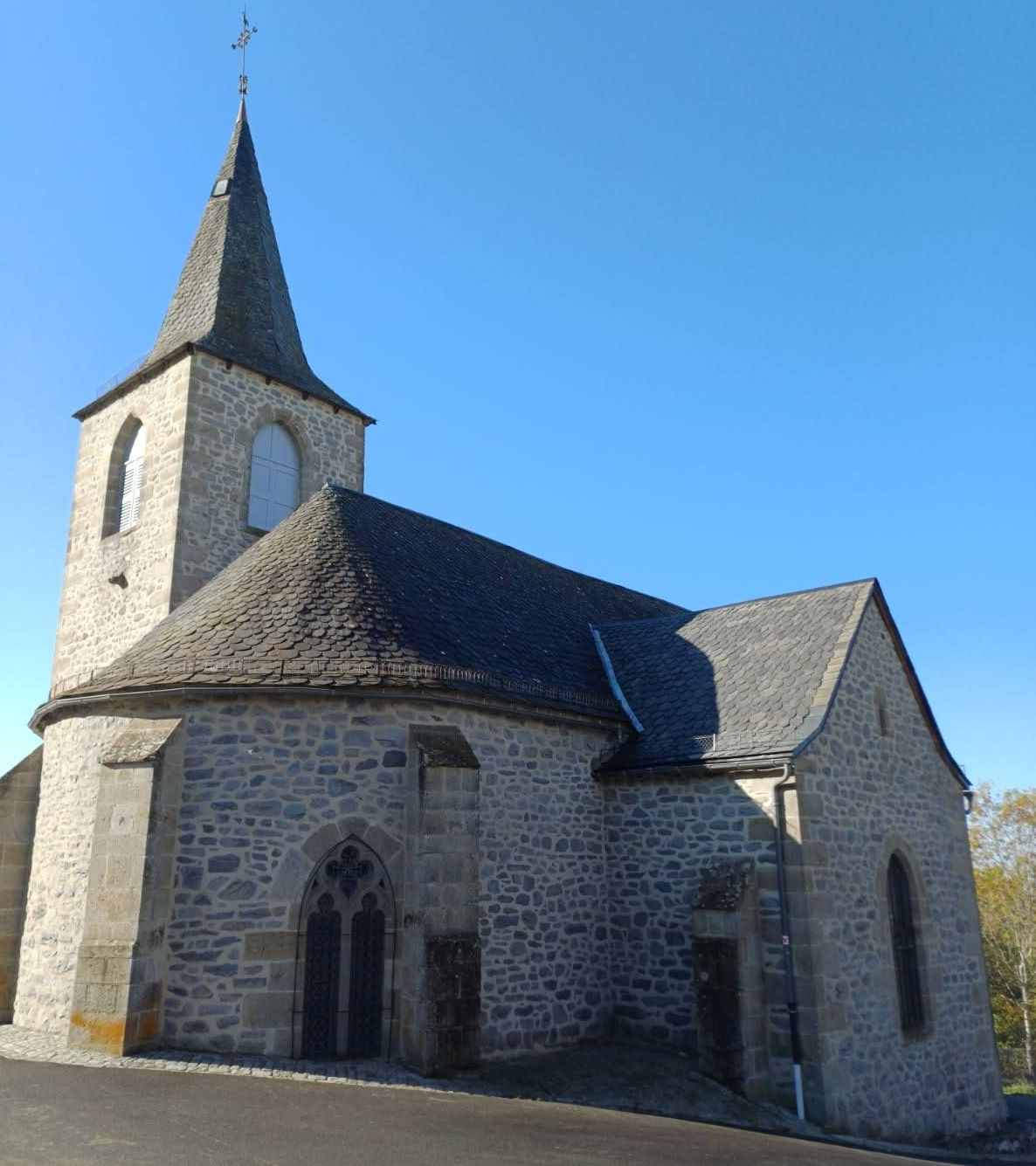 Église en pierre avec un haut clocher se détachant sur un ciel bleu.
