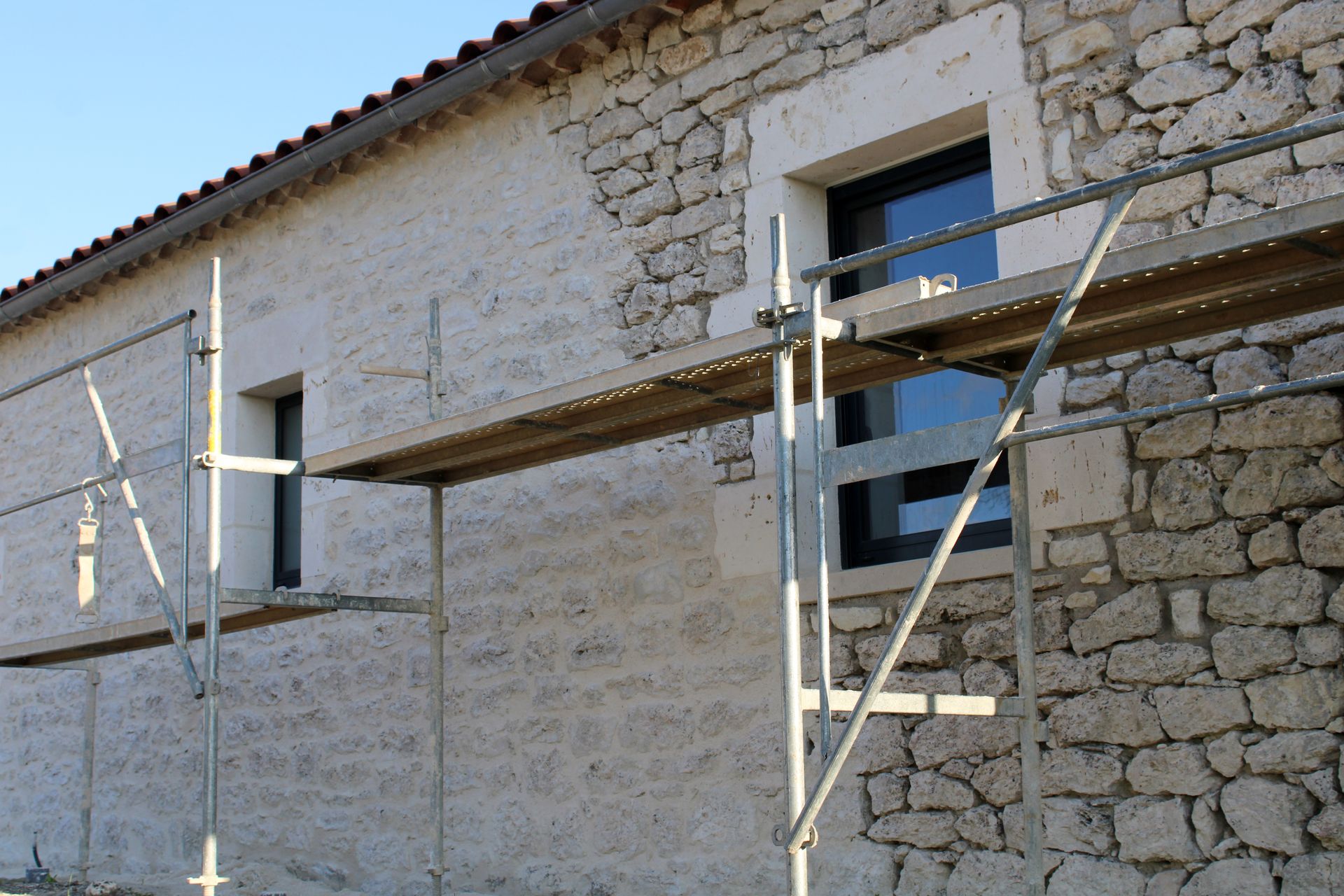Une partie d'un bâtiment en pierre en cours de rénovation extérieure, avec des échafaudages et un mélange de murs bruts et enduits.