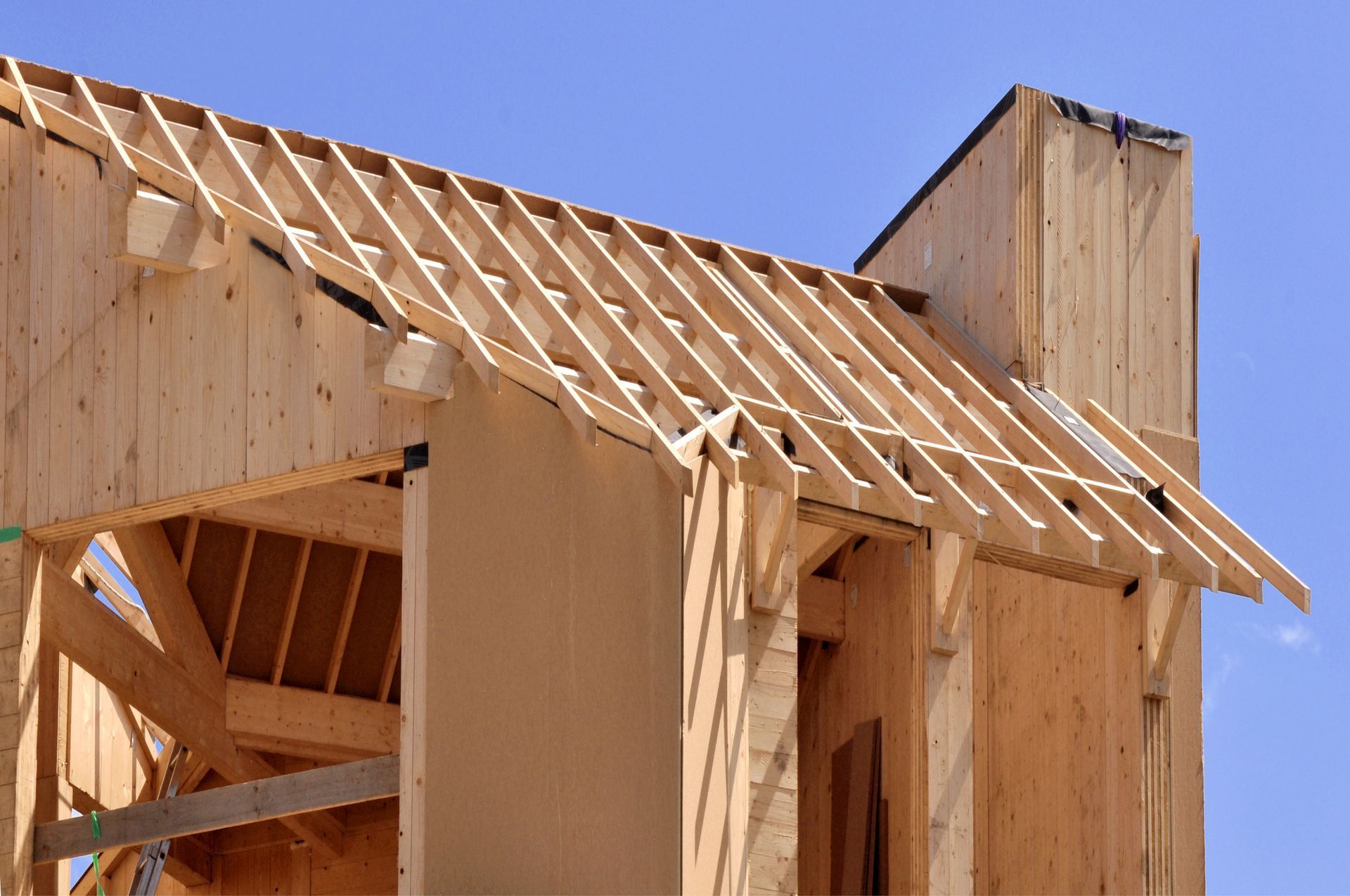 Maison en bois en construction, charpente apparente sur fond de ciel bleu clair.