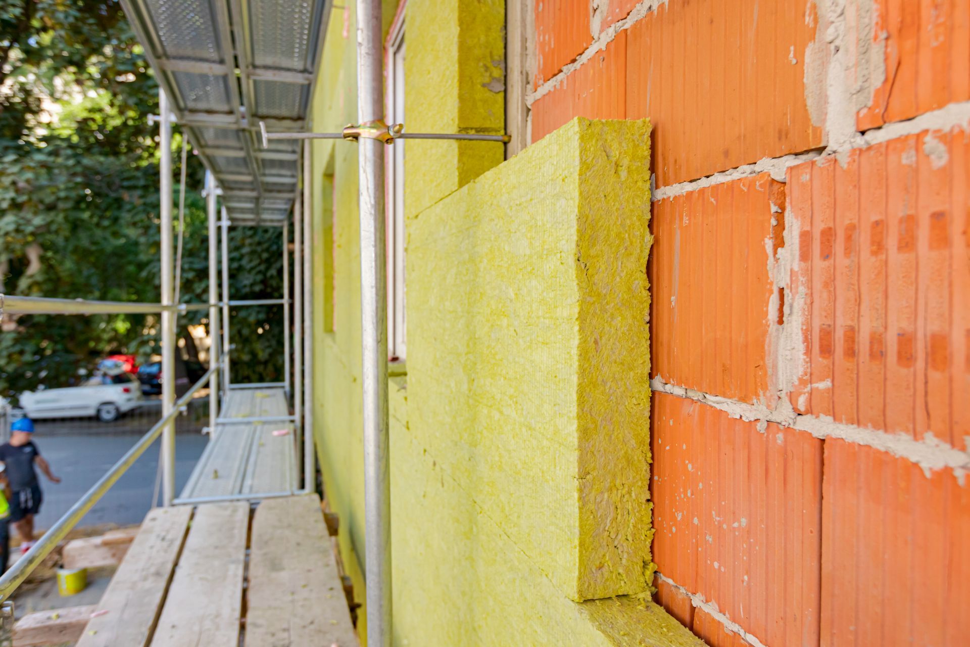 Installation d'isolant sur un mur de briques, avec des échafaudages en arrière-plan.