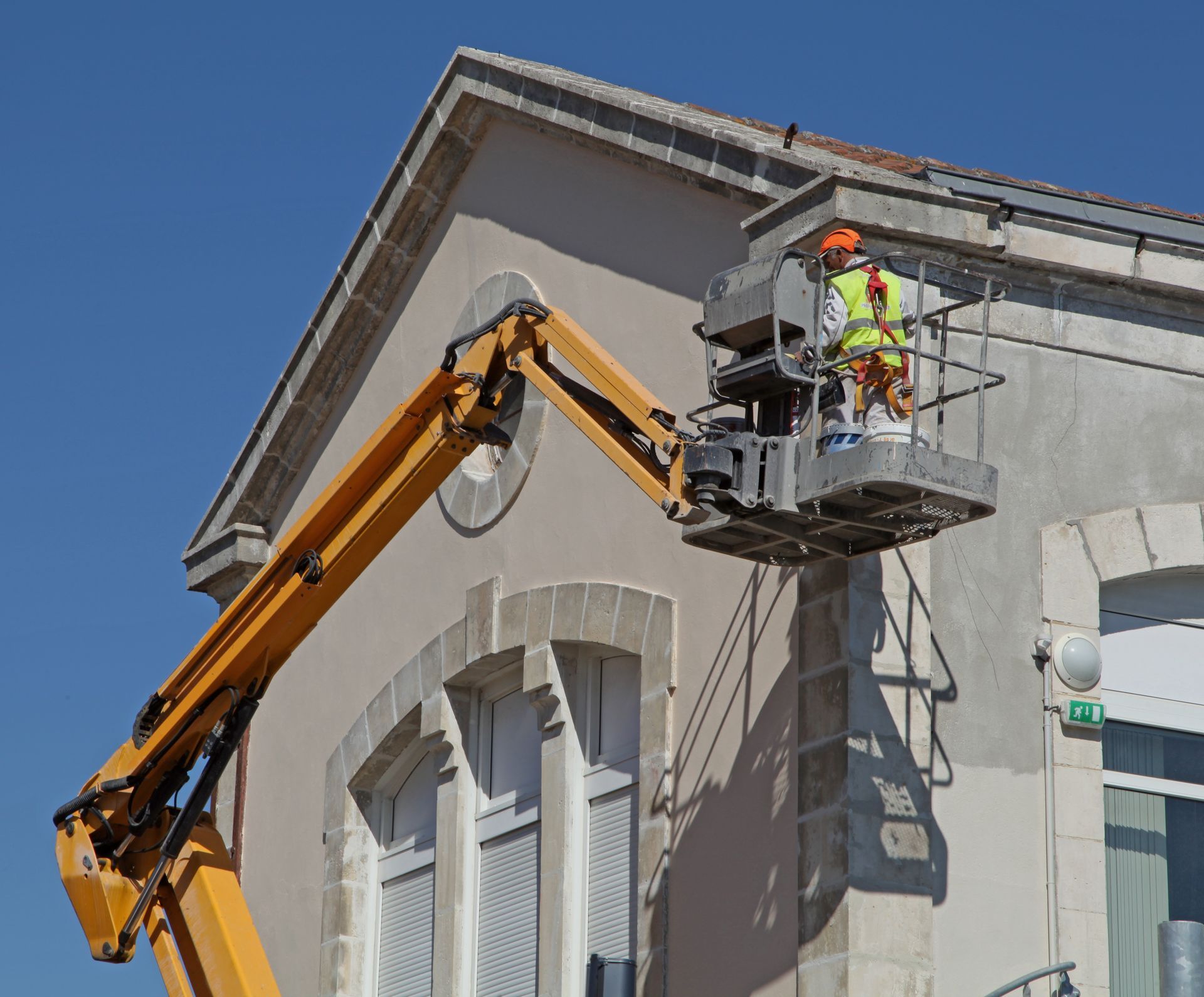 Un ouvrier répare la façade d'un immeuble dans la nacelle d'un ascenseur, par une journée ensoleillée.