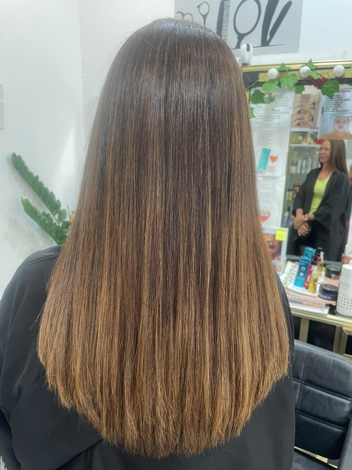 Una mujer con cabello largo está sentada en una silla frente a un espejo.