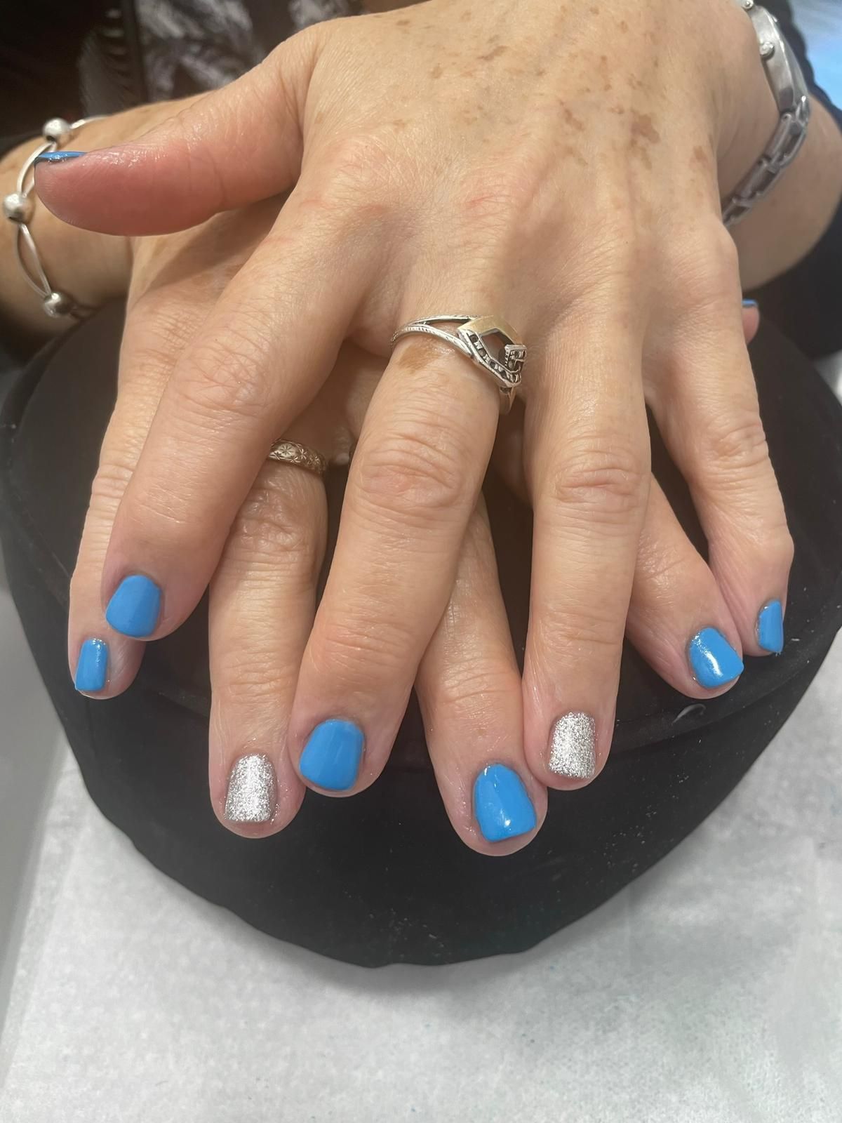 Manos de mujer con uñas azules y un anillo de plata.