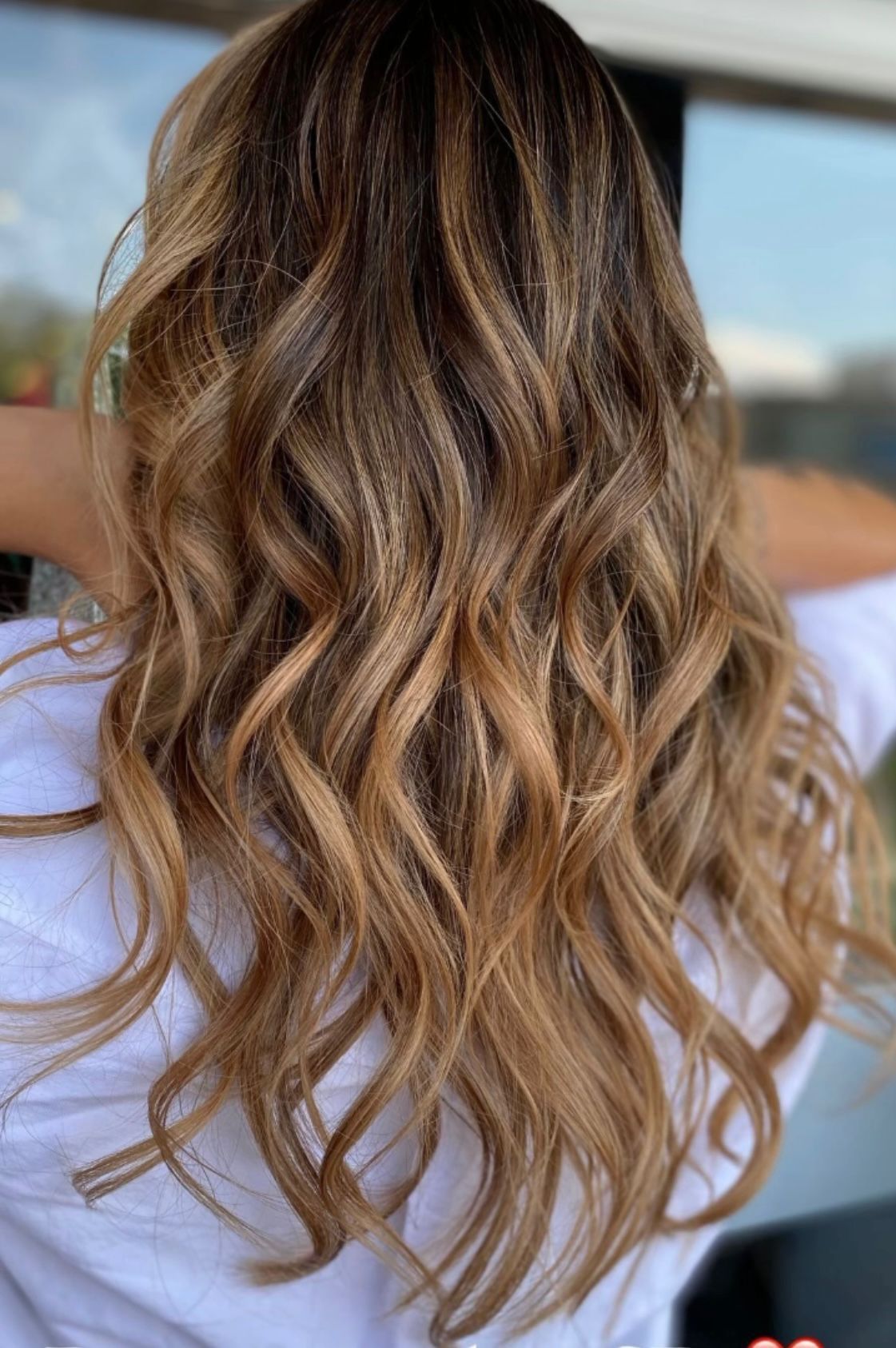 Una mujer con cabello castaño largo y ondulado lleva una camisa blanca.