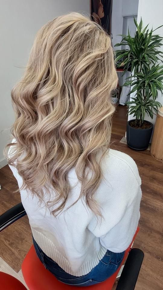 Una mujer con cabello rubio y rizado está sentada en una silla en un salón.