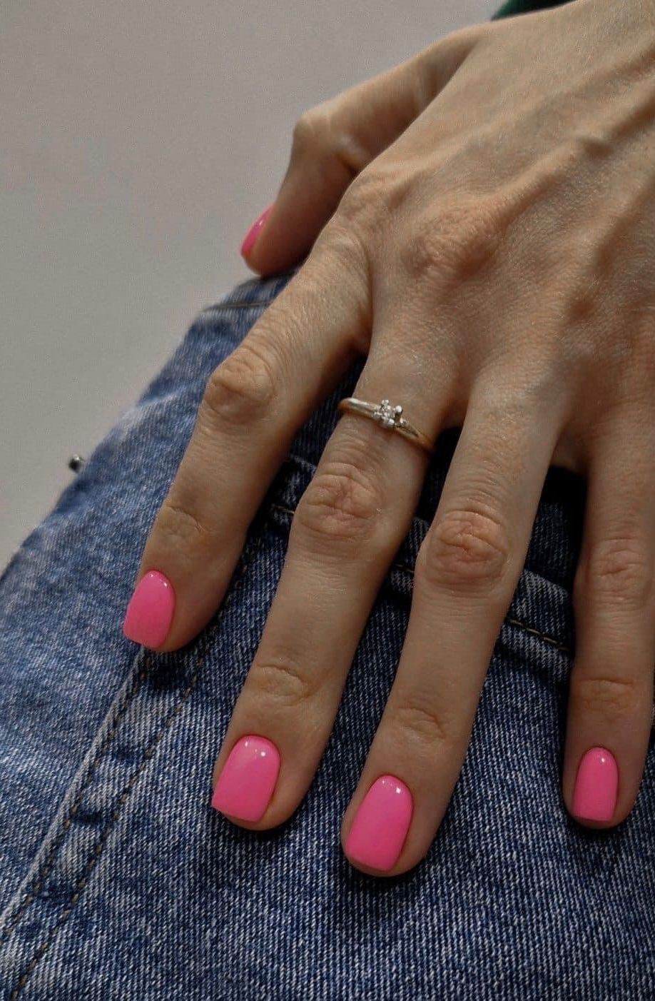 La mano de una mujer con uñas rosas y un anillo en el dedo.