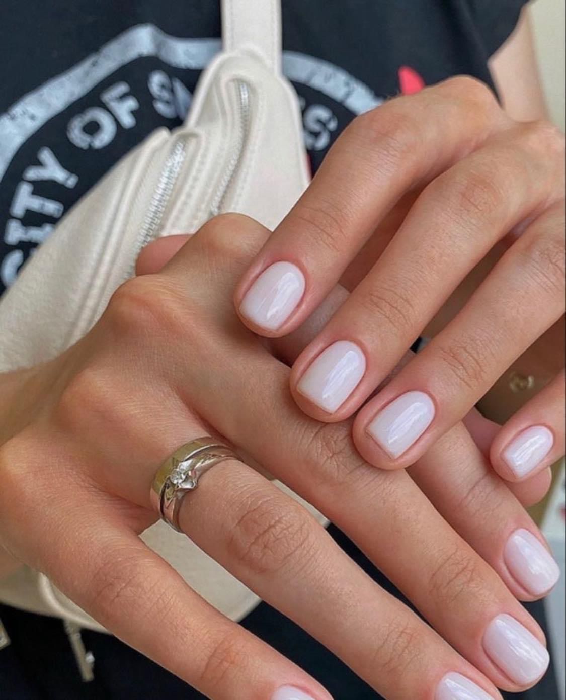 La mano de una mujer con uñas blancas y un anillo en el dedo.