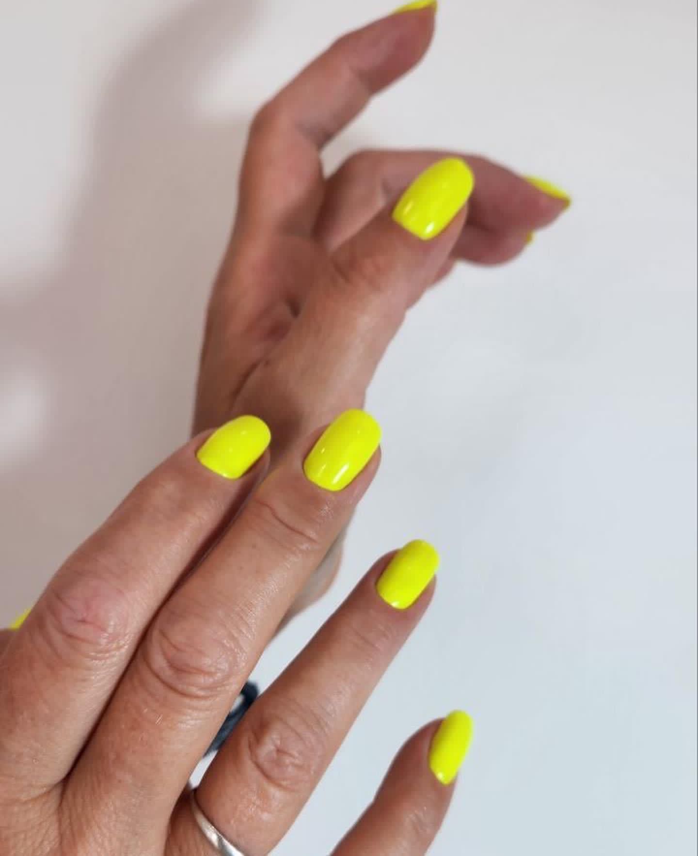 Un primer plano de la mano de una mujer con uñas de color amarillo brillante.