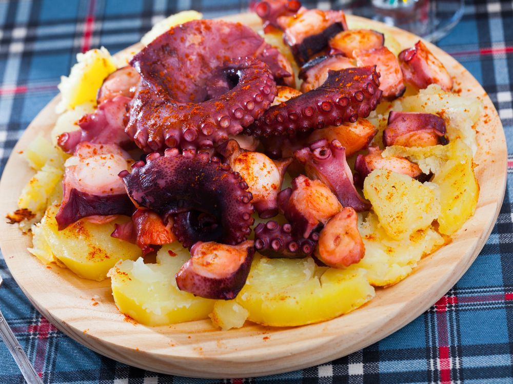 Un plato de pulpo y patatas sobre una tabla de cortar de madera sobre una mesa.