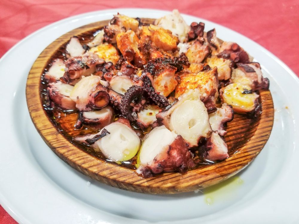 Un plato blanco cubierto con una bandeja de madera de pulpo.