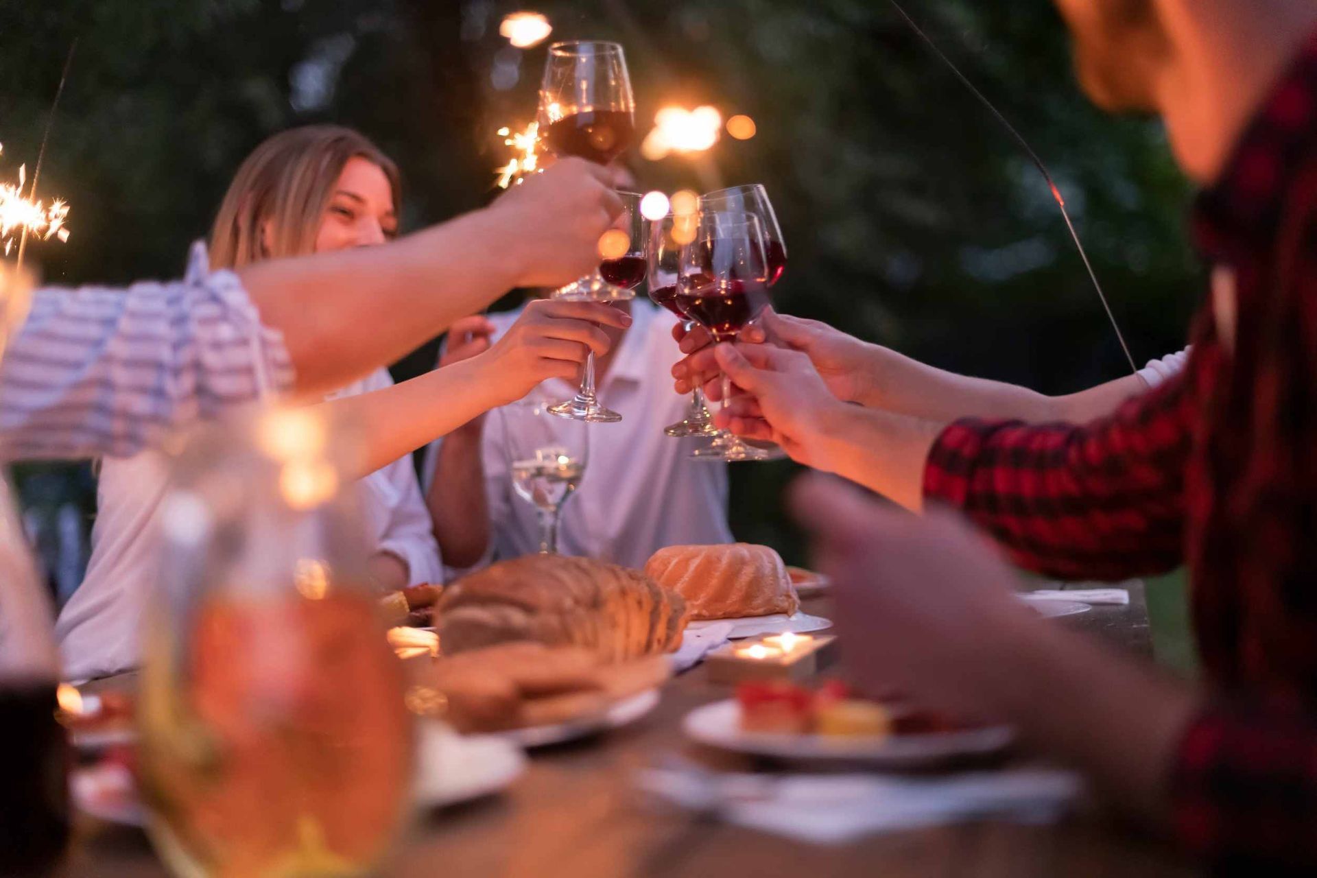 Un grupo de personas están sentadas en una mesa brindando con copas de vino y bengalas.