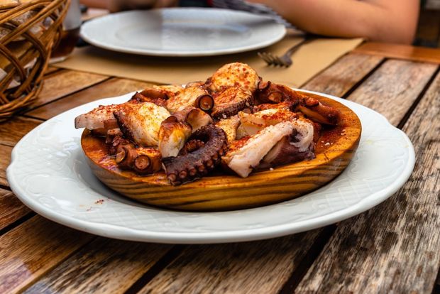 Un plato de pulpo en un plato de madera sobre una mesa de madera.