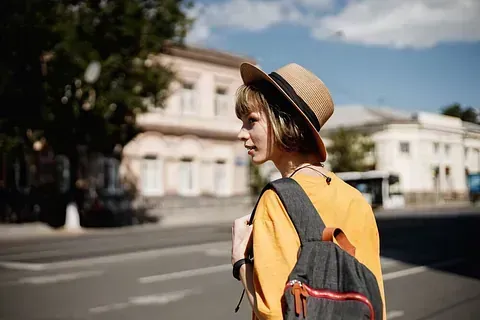 Una mujer que lleva un sombrero y una mochila camina por la calle.
