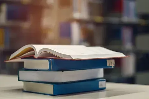 Una pila de libros colocados uno encima del otro sobre una mesa en una biblioteca.