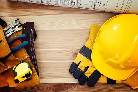 Un casco, guantes, herramientas y un plano sobre una mesa de madera.