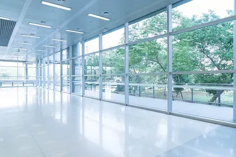 Una gran habitación vacía con muchas ventanas y árboles al fondo.