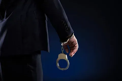 Un hombre con traje sostiene un par de esposas en su mano.