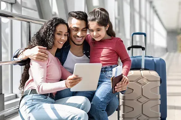 Una familia está sentada en un banco en un aeropuerto mirando una tableta.