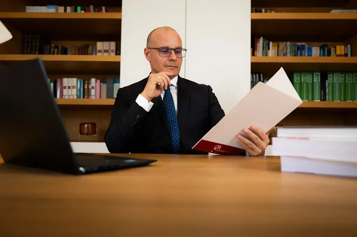 Un hombre con traje y corbata está sentado en un escritorio leyendo un libro.