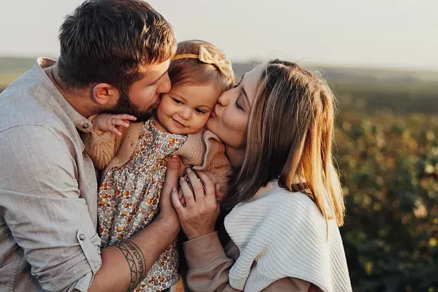 Una hombre y una mujer al lado de una niña dándole un beso.