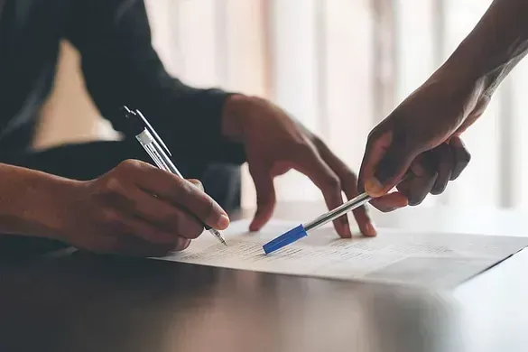 Un hombre y una mujer están firmando un documento en una mesa.
