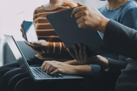Un grupo de personas están sentadas en una fila usando computadoras portátiles y tabletas.