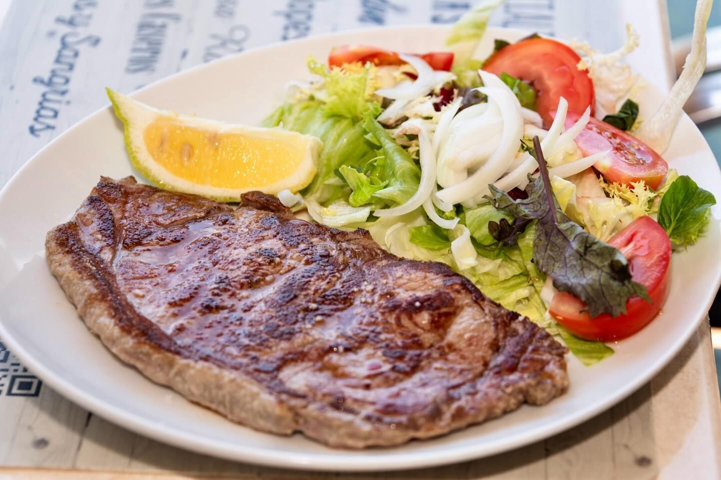 Un plato blanco cubierto con un filete y una ensalada.