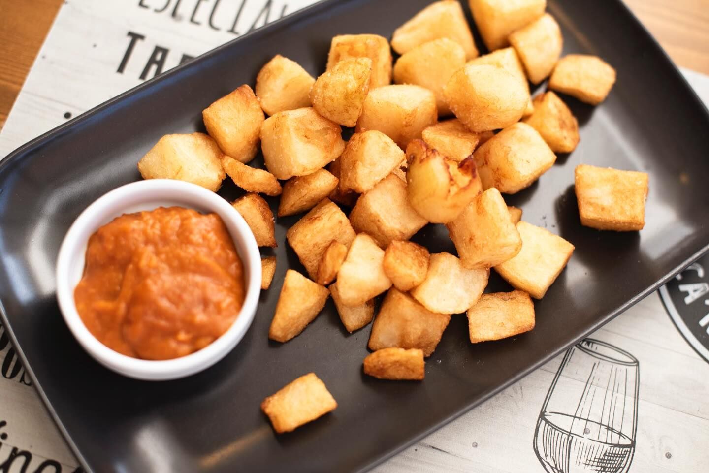 Un plato negro cubierto con patatas fritas y un tazón pequeño de salsa.