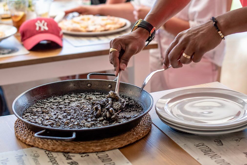 Una persona sostiene un tenedor sobre una sartén con comida sobre una mesa.