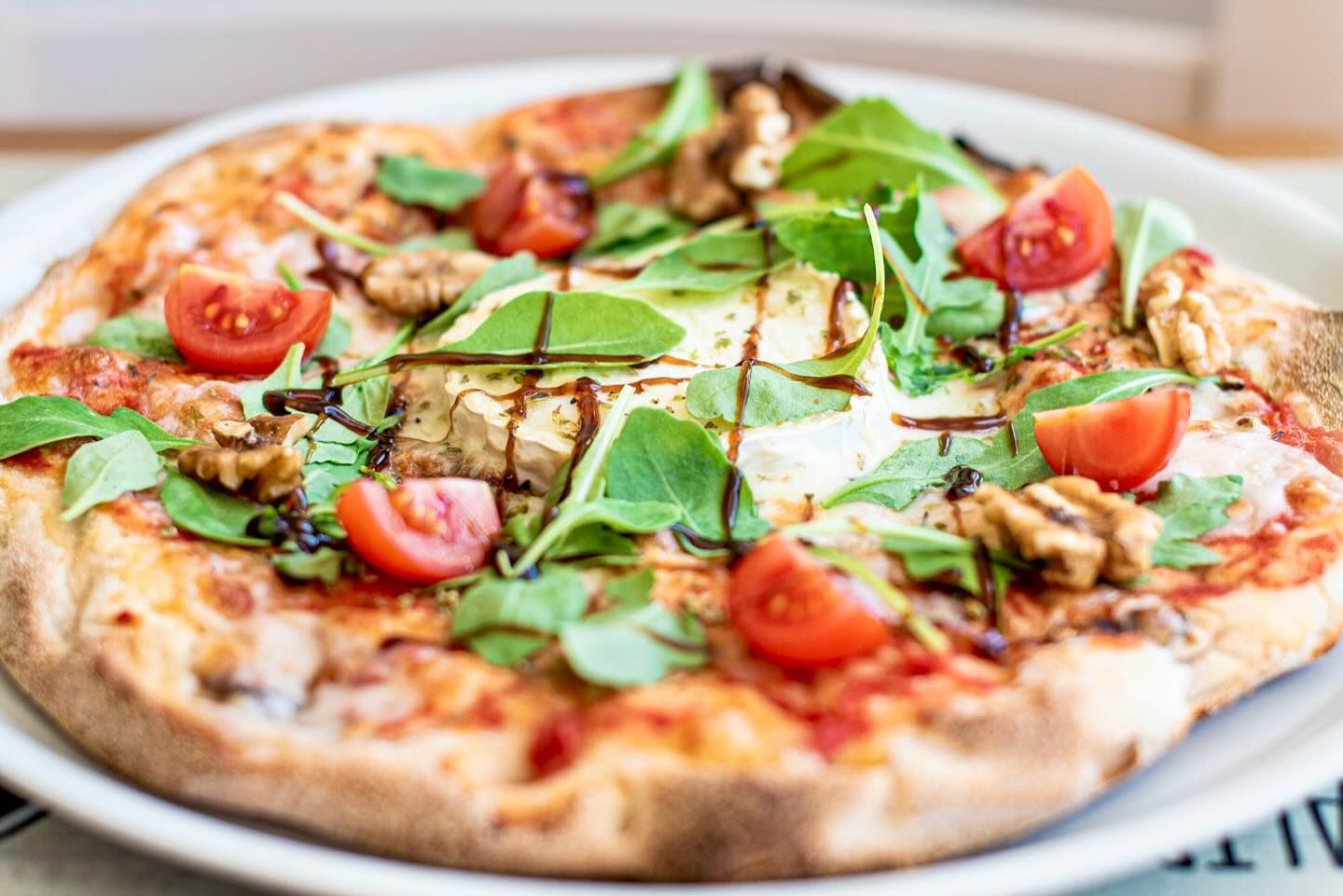 Una pizza con tomates, champiñones y verduras en un plato blanco.