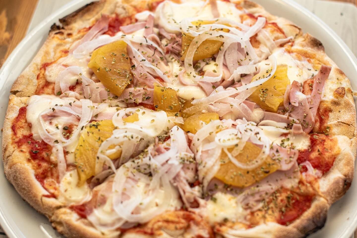 Una pizza con jamón, piña, cebolla y queso en un plato blanco.