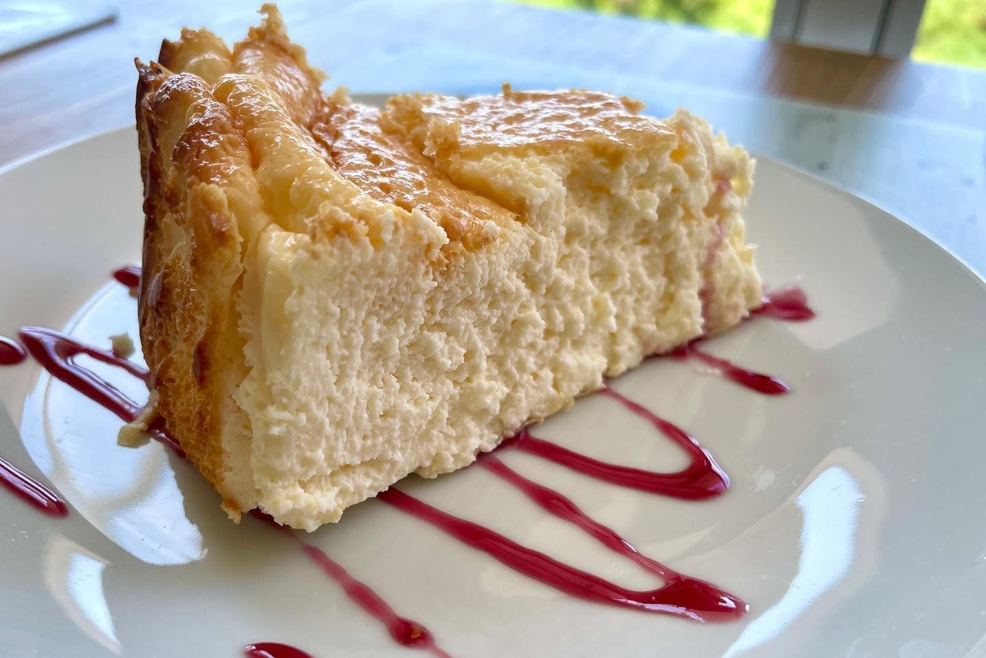 Una rebanada de tarta de queso con salsa de frambuesa en un plato blanco.