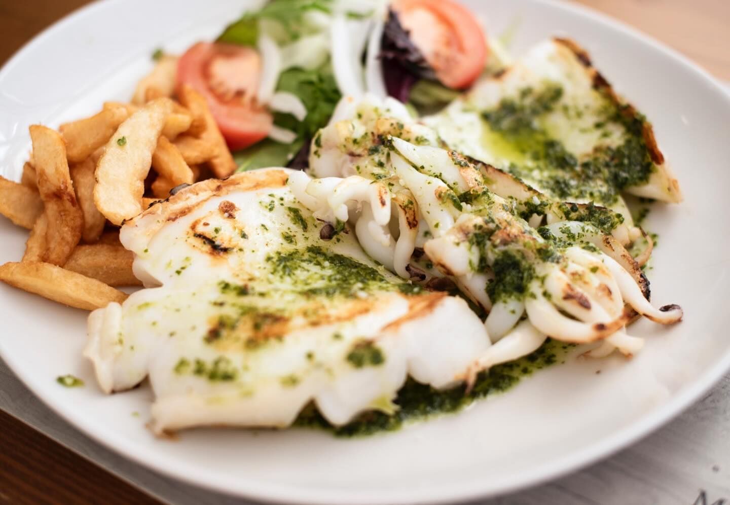Un plato blanco cubierto con calamares a la parrilla y patatas fritas.