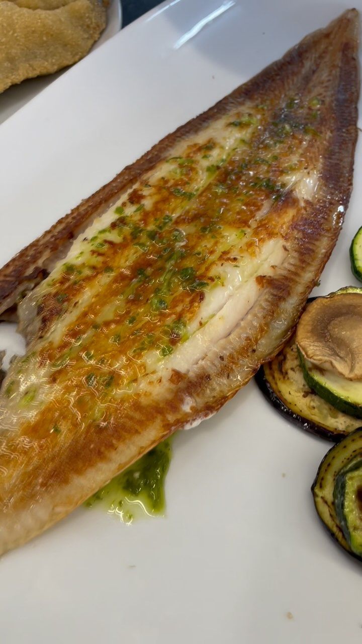 Un plato blanco cubierto con un trozo de pescado y verduras.
