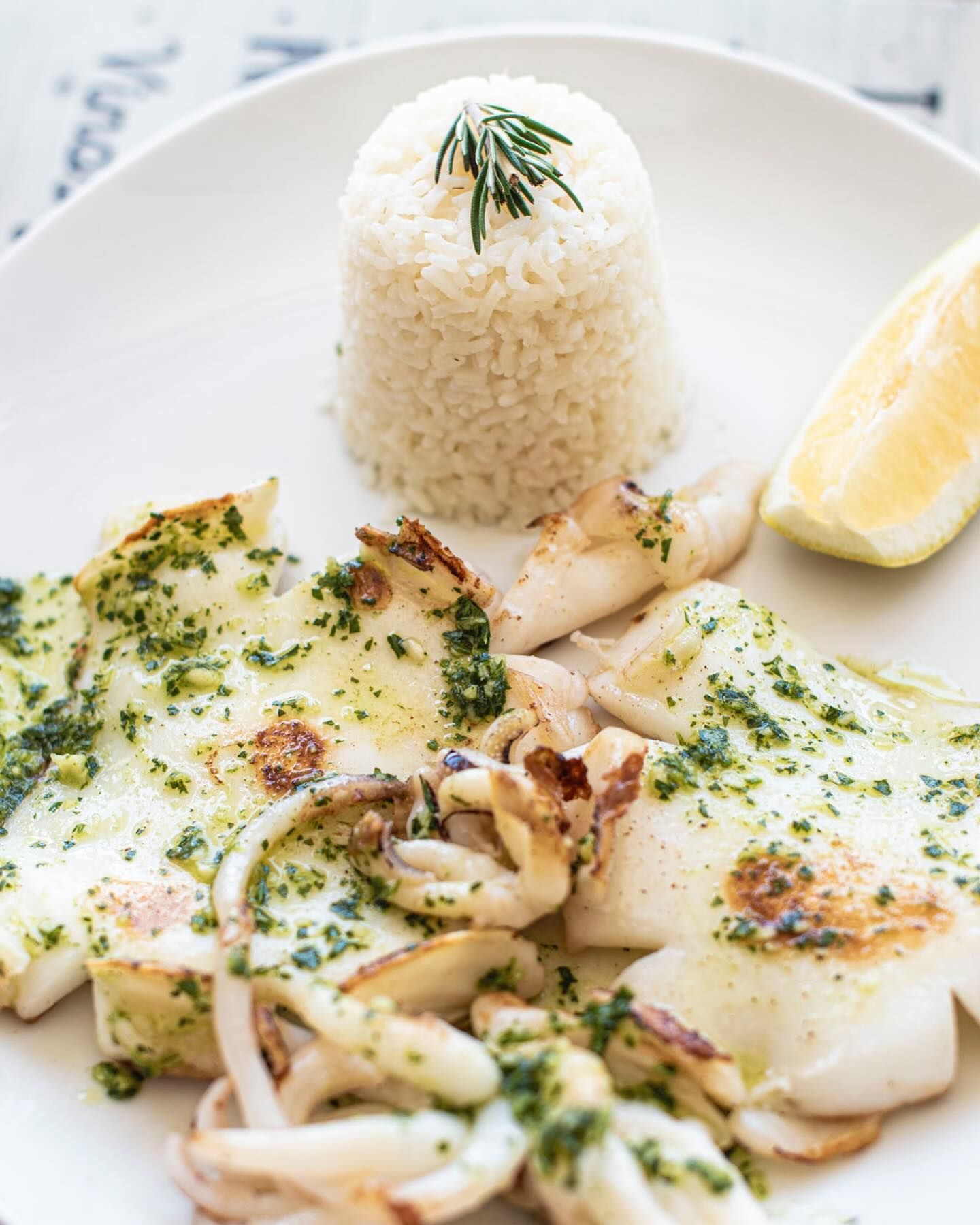 Un plato blanco cubierto con calamares, arroz y una rodaja de limón.