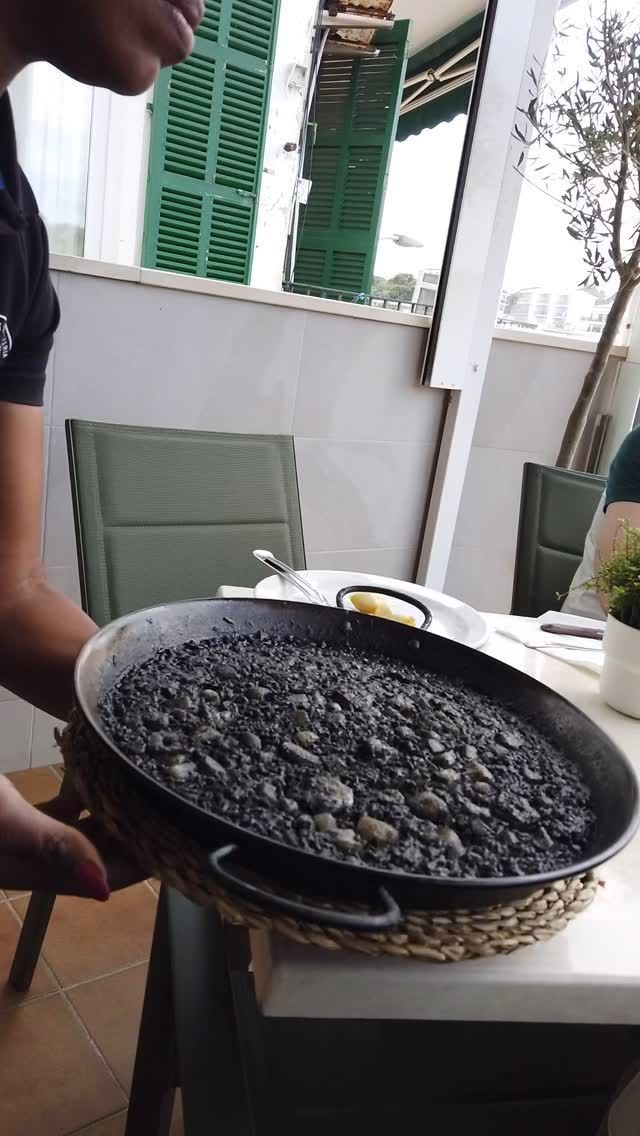 Un hombre sostiene una sartén con arroz negro sobre una mesa.