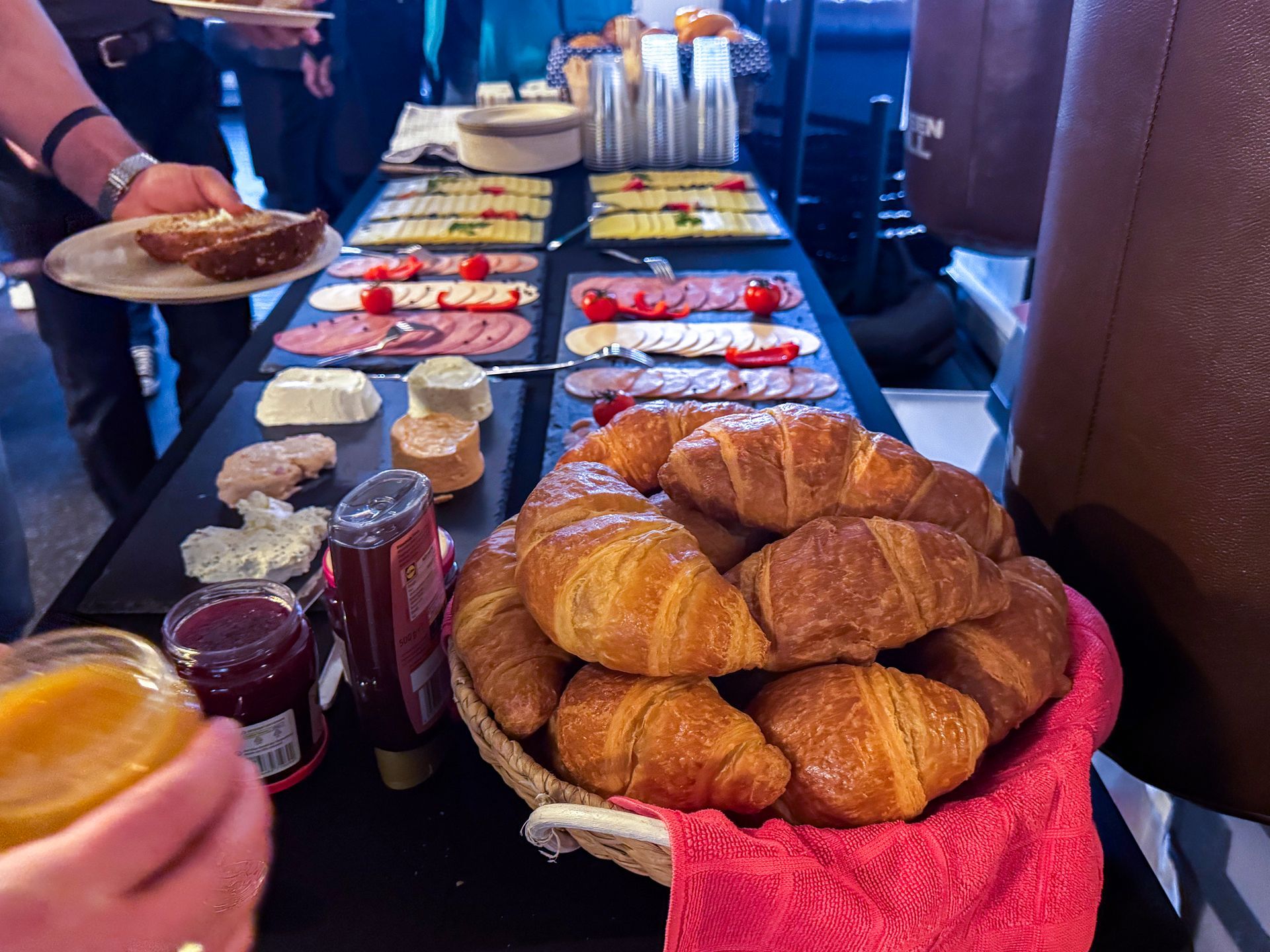 Ein Tisch gedeckt mit Käse, Wurst, Marmelade, Brötchen und mehr.