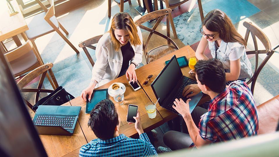 Eine Gruppe von Leuten sitzt mit Laptops und Tablets um einen Tisch.