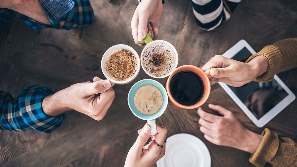 Eine Gruppe von Leuten sitzt mit Tassen Kaffee an einem Tisch.