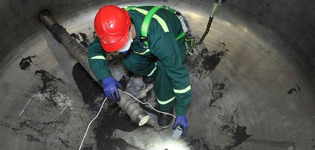 Un hombre con un casco rojo está trabajando en una tubería en un tanque.