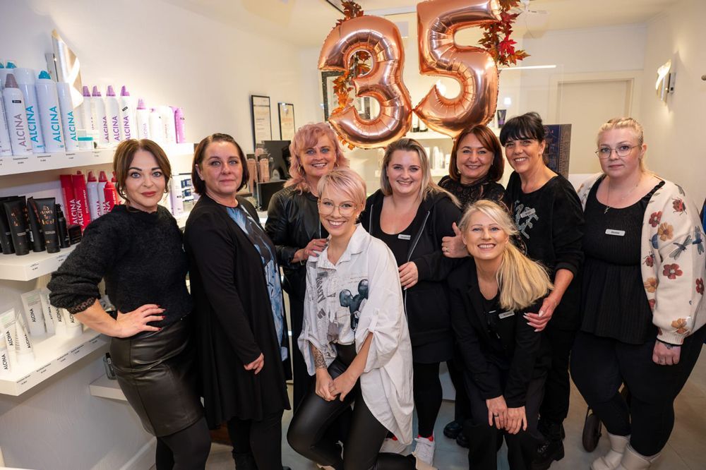 Eine Gruppe von Frauen feiert in einem Friseursalon das 35-jährige Jubiläum; roségoldene Luftballons.