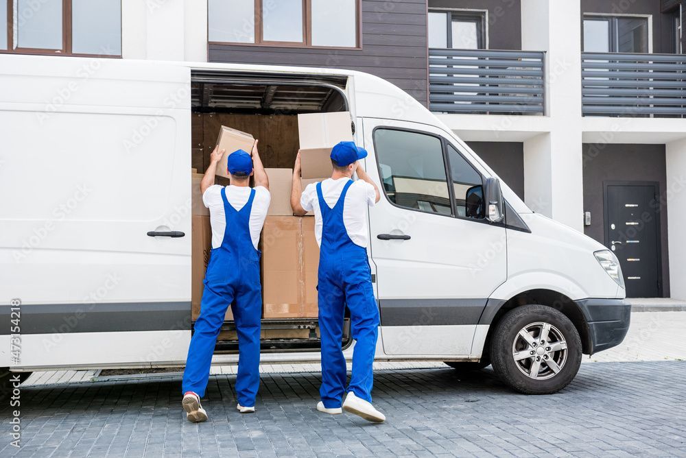 Zwei Möbelpacker laden Kisten in einen weißen Lieferwagen.