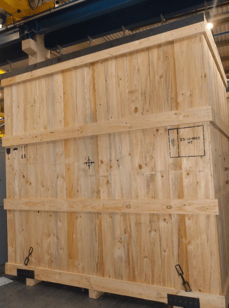 Gran caja de madera con refuerzos metálicos en un almacén industrial.