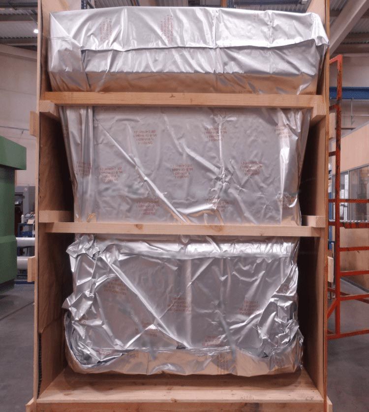 Tres cajas isotérmicas envueltas en papel de aluminio apiladas dentro de una caja de madera en un almacén.