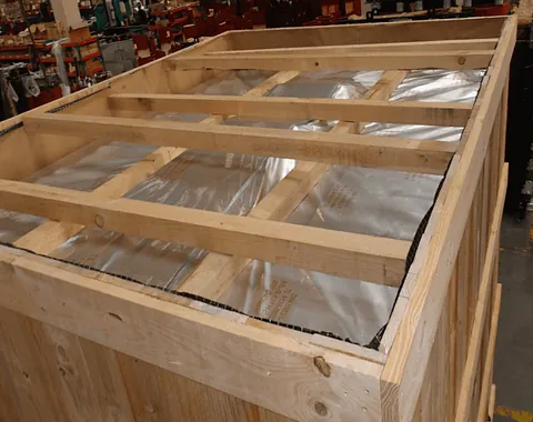 Caja de madera con tapa enmarcada y cubierta de plástico transparente, ubicada en un taller o almacén.
