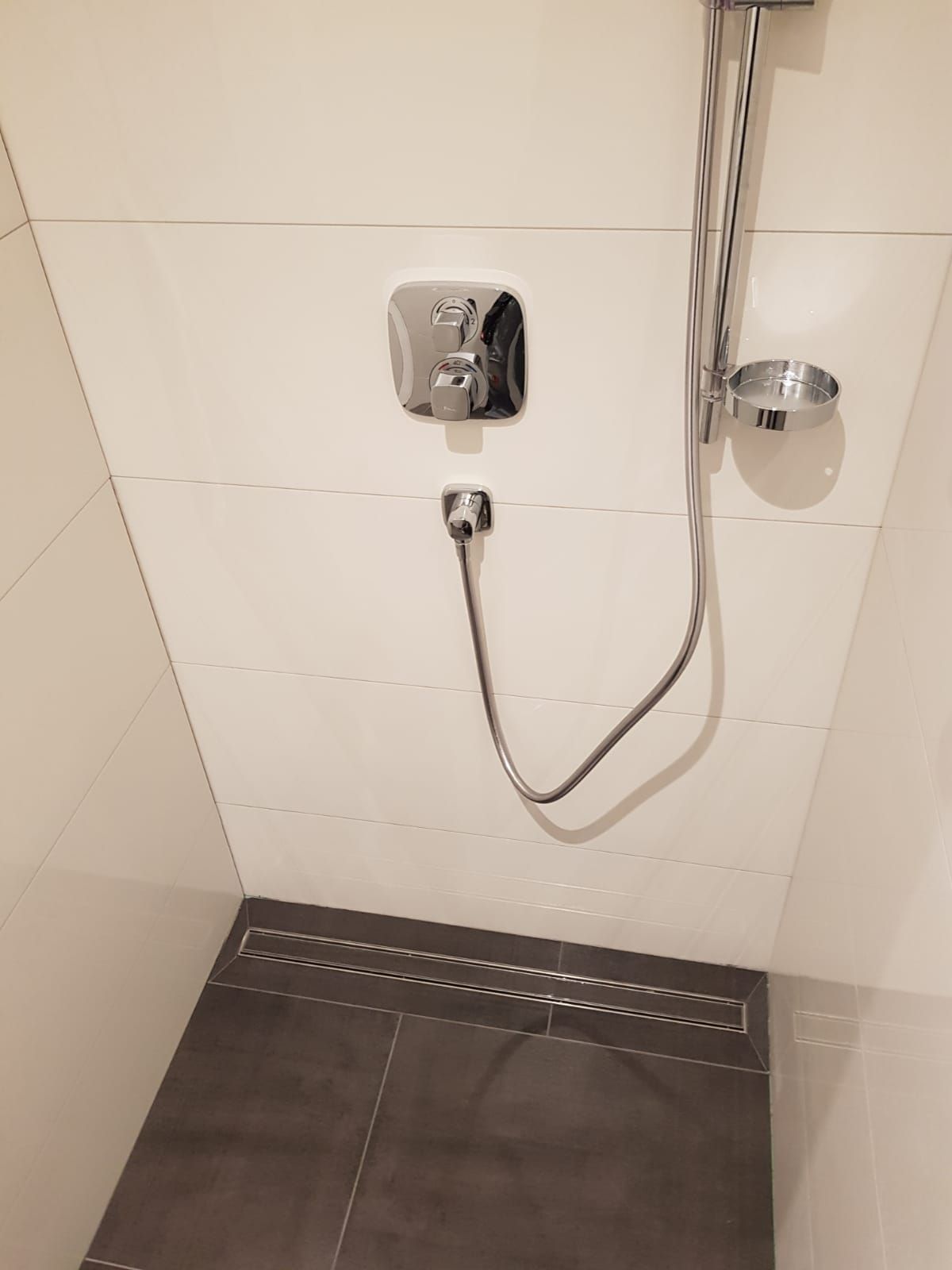 Bodengleiche Dusche mit weißen Wandfliesen und braunen Bodenfliesen