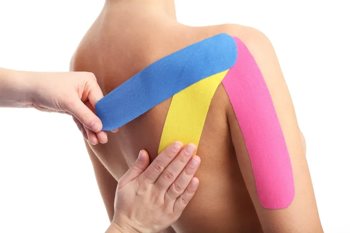 Un profesional aplica cinta kinesiológica de colores en el hombro y la parte superior de la espalda de una persona.